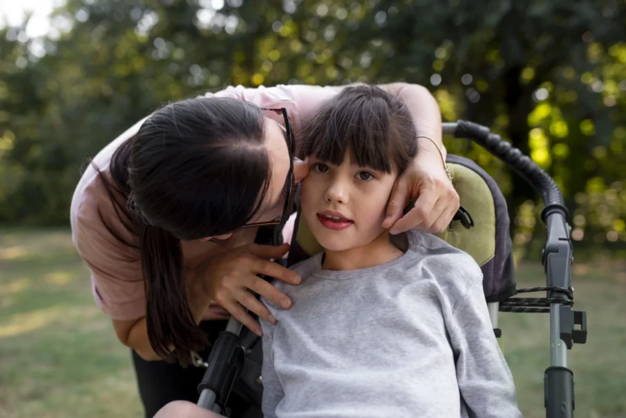 Woman kissing on the cheek of a female child in a wheelchair